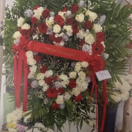 Heart-shaped funeral wreath with red and white flowers and a red ribbon