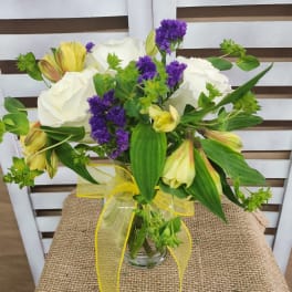 Bouquet of white roses, purple filler flowers, and yellow alstroemeria in a glass vase