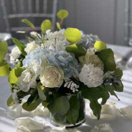 White and pale blue floral centerpiece in a glass vase