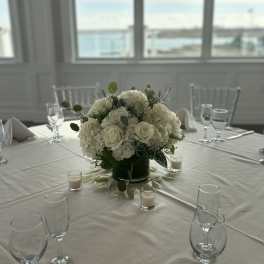 White rose and hydrangea centerpiece in a dark vase on a table