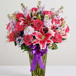 Bouquet of pink roses and lilies in a clear glass vase with a purple ribbon