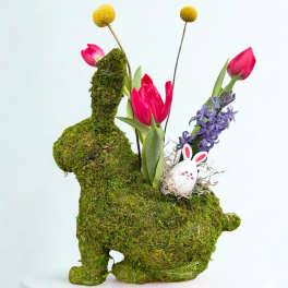 Moss-covered bunny-shaped floral display with pink tulips, purple hyacinth, and a small bunny egg