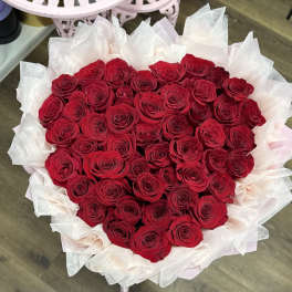 Heart-shaped bouquet of red roses wrapped in pale pink and white tissue paper