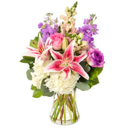 Bouquet of pink lilies, roses, and purple flowers in a clear glass vase