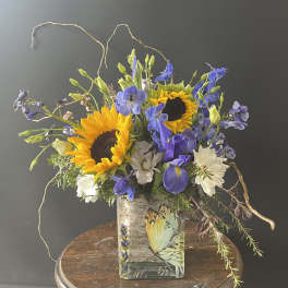 Bouquet of sunflowers, blue flowers, and white daisies in a glass vase