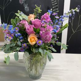 Mixed bouquet of pink, peach, and blue flowers in a glass vase