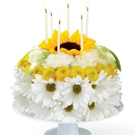 Daisy and sunflower cake with lit candles on a pedestal stand
