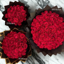 Three bouquets of tightly clustered red roses in different sizes wrapped in dark paper on a marble surface.