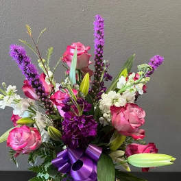 Pink roses and purple flowers arranged with a purple ribbon