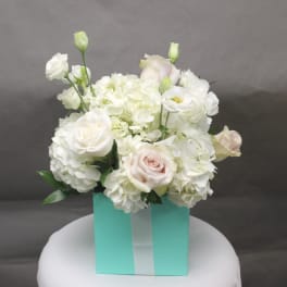 White roses and hydrangeas arranged in a turquoise gift box with a ribbon