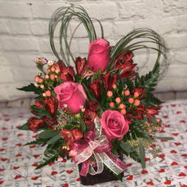 Pink roses and red alstroemeria in a black vase with a ribbon bow