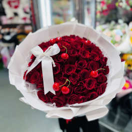 Round bouquet of deep red roses with faux cherries and a white bow in white paper wrapping