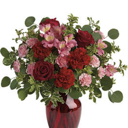 Red and pink roses, carnations, and alstroemeria arranged in a red glass vase