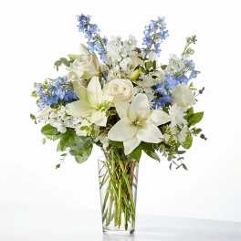 White roses and lilies with blue flowers in a clear glass vase