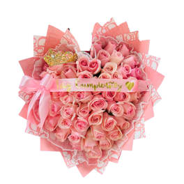 Heart-shaped bouquet of pink roses with birthday ribbon, pink bow, and a decorative gold crown accent.