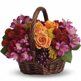 Basket of orange roses, purple alstroemeria, red mums, and grapes in a woven brown basket