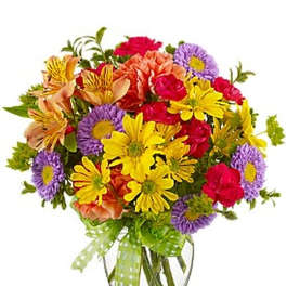 Bright mixed bouquet of yellow daisies, purple asters and pink and peach blooms in a clear vase with green ribbon.