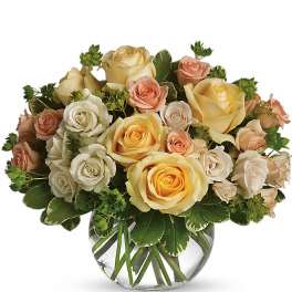 Round glass vase filled with yellow, cream, and peach roses.