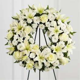 White floral wreath on a black stand with lilies, roses, and daisies