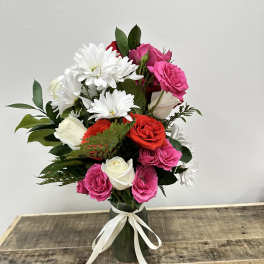 Pink, red, and white roses with white daisies in a vase tied with ribbon.