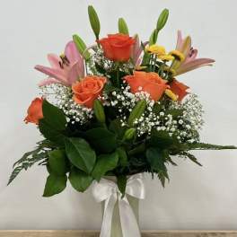 Orange roses and pink lilies in a white vase with a ribbon