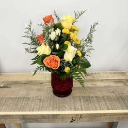 Mixed roses and yellow flowers in a red glass vase
