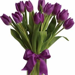 Bouquet of purple tulips in a clear glass vase with a matching purple ribbon bow