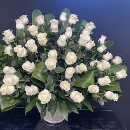 White roses arranged in a vase with broad green leaves