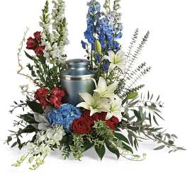 Sympathy arrangement of red, white, and blue flowers surrounding a metallic cremation urn