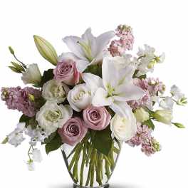 Pastel arrangement of white lilies and soft pink and white roses in a clear glass vase