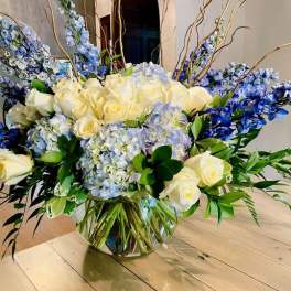 Large bouquet of cream roses, blue flowers, and hydrangeas in a glass vase