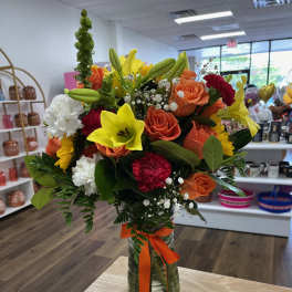 Mixed bouquet of orange roses, yellow lilies, and white carnations in a glass vase