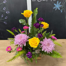 Mixed bouquet with yellow roses, lavender chrysanthemums, and purple blooms in a wooden container