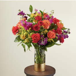 Mixed bouquet of roses, carnations, and purple flowers in a glass vase