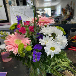 Mixed bouquet with pink gerberas, white daisies, and purple filler flowers in a glass vase