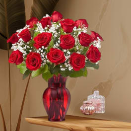 Red roses arranged in a red glass vase with white filler flowers