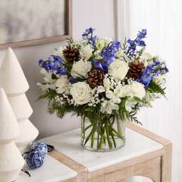 White and blue floral arrangement in a clear glass vase with pinecones