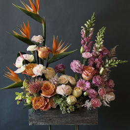 Tall floral arrangement with orange birds of paradise and pink roses in a wooden container