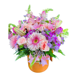 Pink and purple mixed flower arrangement with gerbera daisies, roses, tulips, and lilies in an orange cylinder container