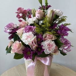 Pink and purple mixed bouquet in a woven basket with a pink ribbon