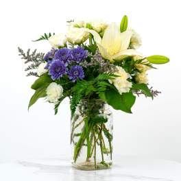 White lilies and purple daisies in a glass jar vase