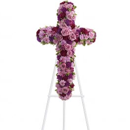 Standing cross-shaped spray of lavender roses and purple flowers on a white easel