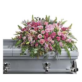 Pink roses, lilies, and other blooms arranged as a spray on a silver casket
