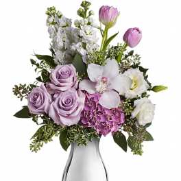 Arrangement of lavender roses, pink tulips, white orchid, and hydrangea in a silver vase
