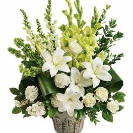 Tall arrangement of white lilies, roses, and carnations with green accents in an ivory urn-style vase
