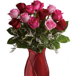 Red and pink rose bouquet in a red glass vase with white filler flowers