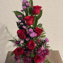 Red roses and purple flowers in a clear glass vase