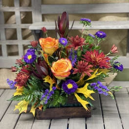 Autumn floral arrangement with orange roses and purple daisies in a wooden box