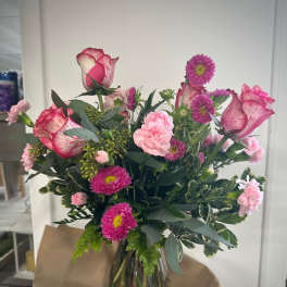 Bouquet of pink roses, carnations, and purple daisies in a glass vase
