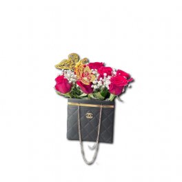 Red roses and white filler flowers arranged in a black quilted handbag with gold butterfly accents.